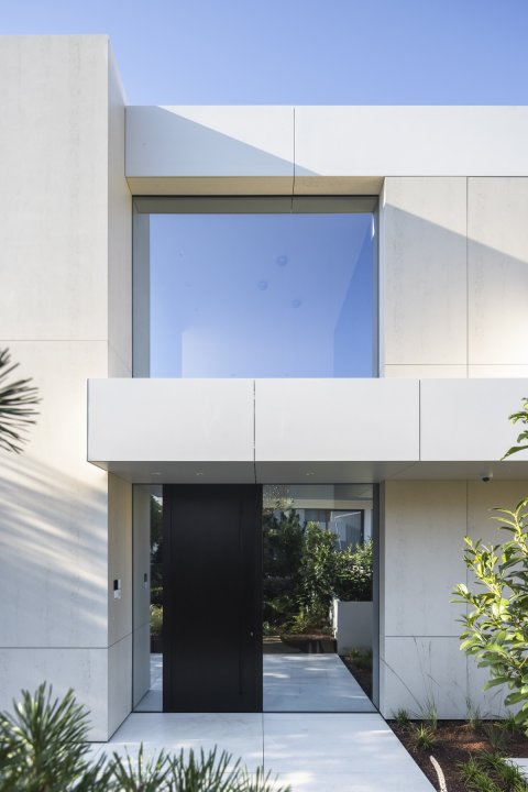 Moderne Hausfassade mit einer schwarzen Eingangstür und einem grossen quadratischen Fenster im Obergeschoss.